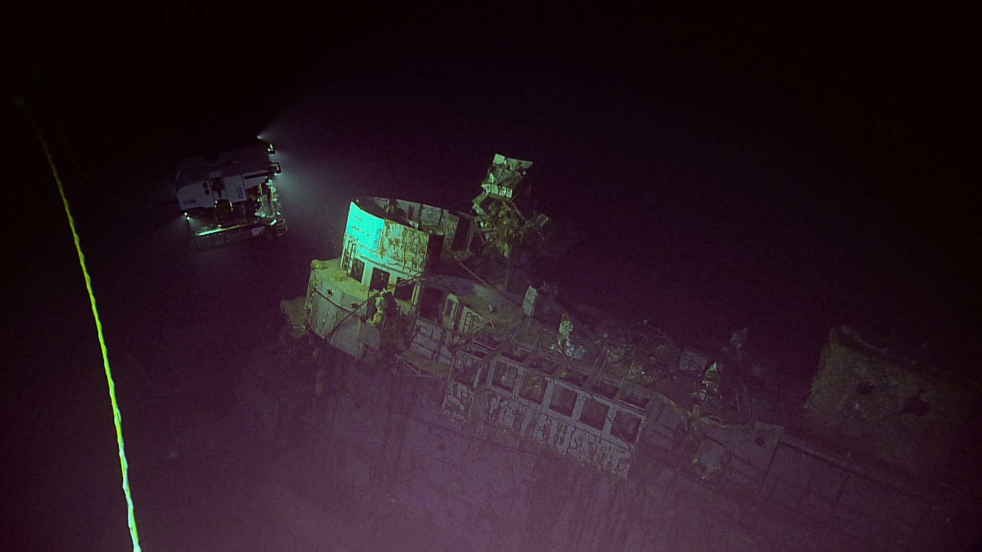 An ROV documenting a submerged wreck, illuminated against dark water